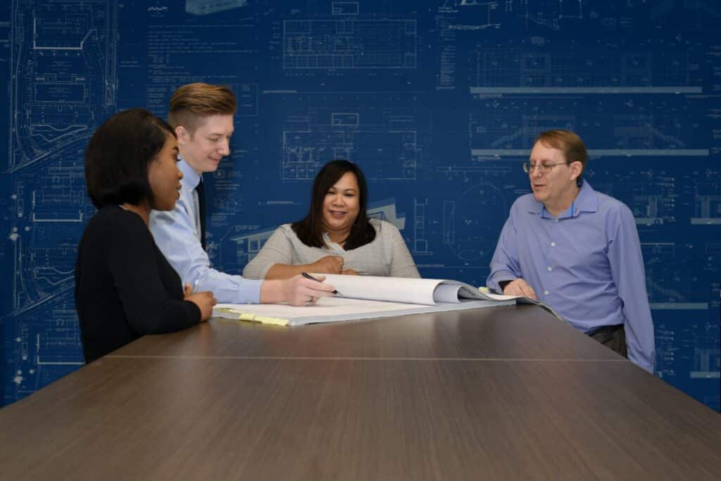 A group of people sitting around a table in front of blueprints.