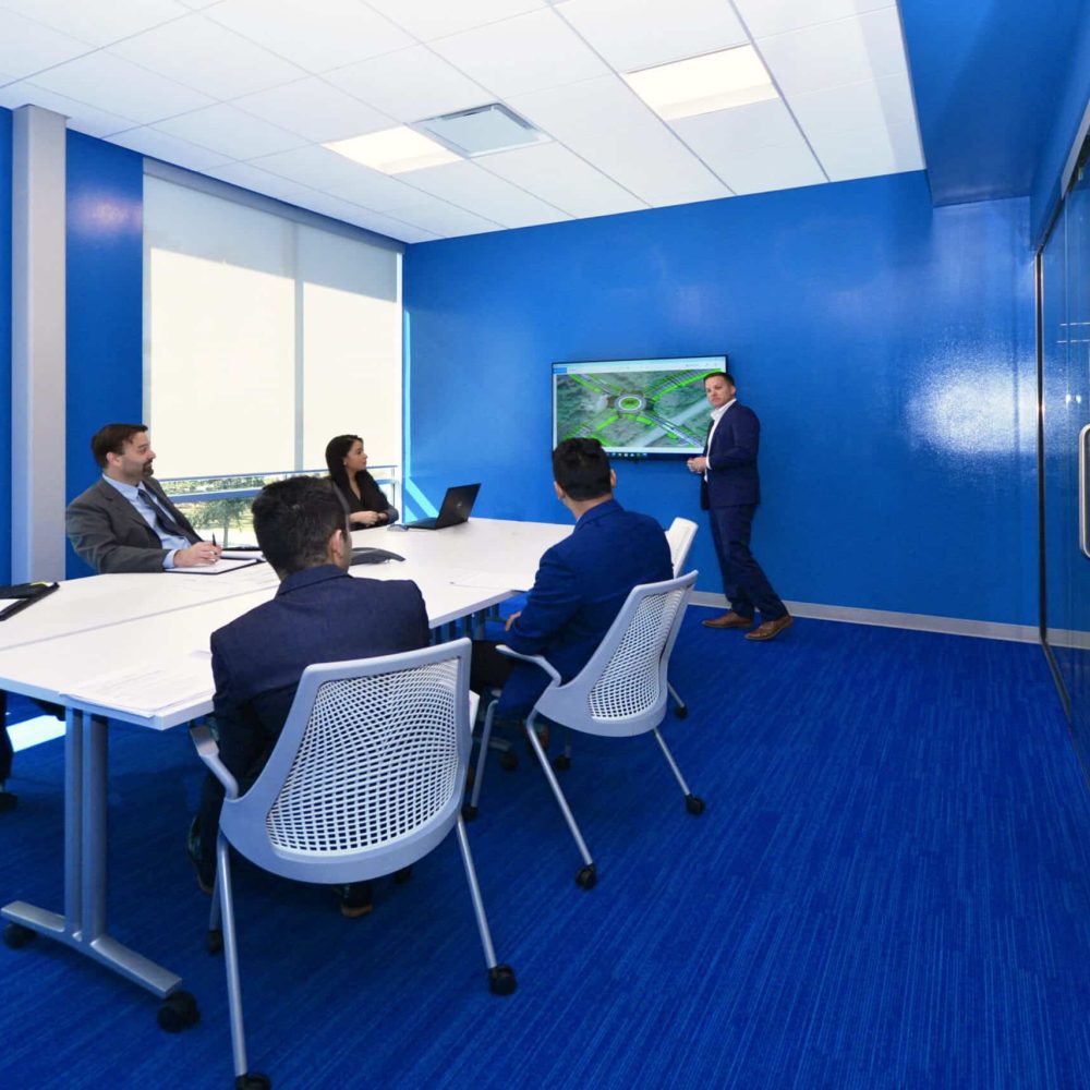 A conference room with blue walls and people sitting around a table.
